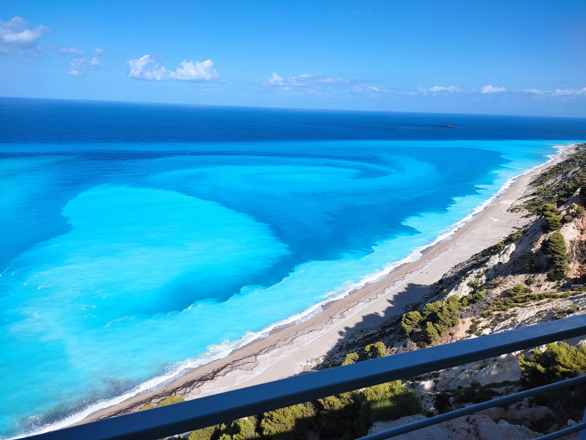 Bright turquoise ocean with a sandy shoreline and rocky coast under a clear blue sky