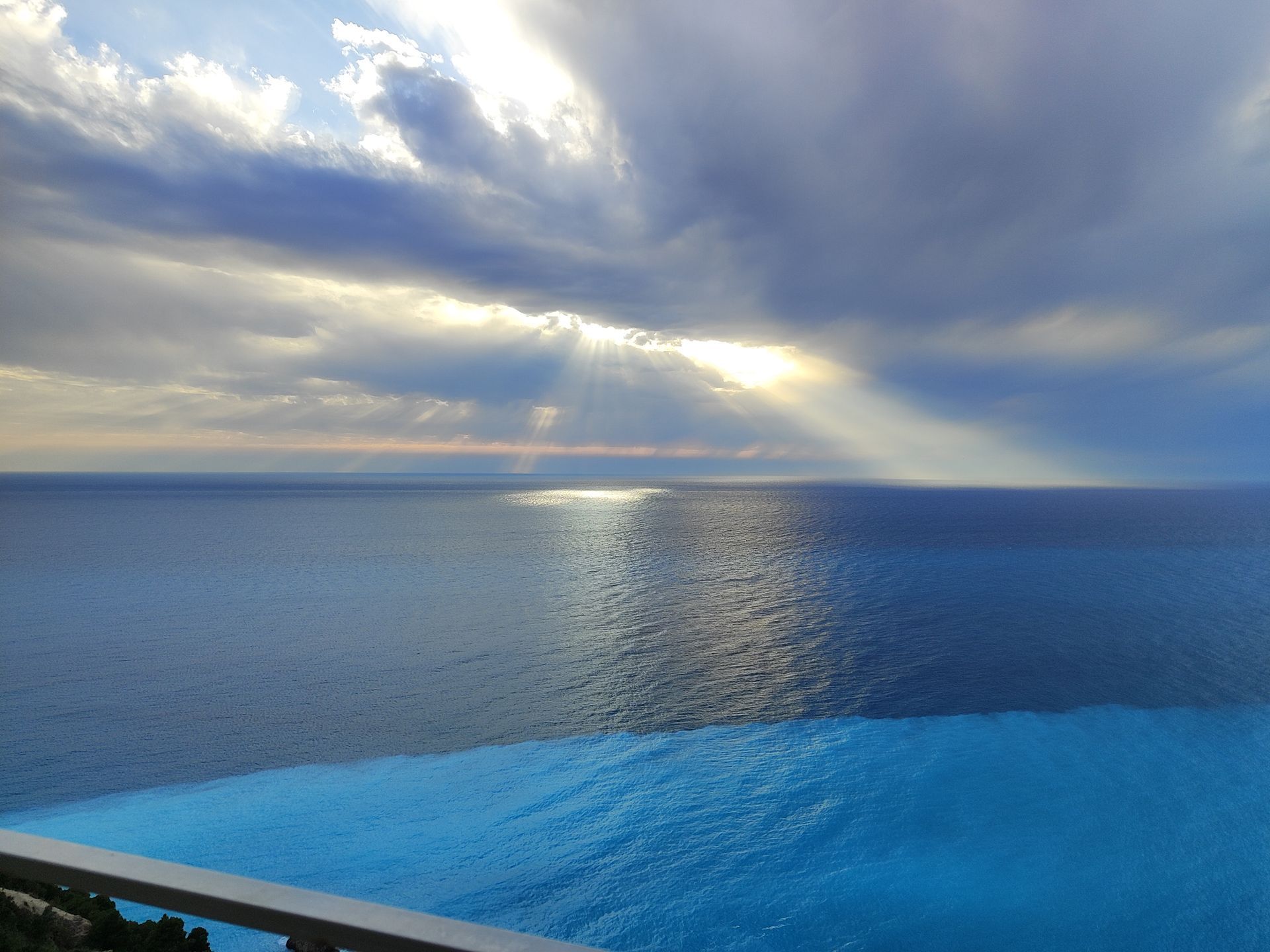 Sunlight breaking through clouds over a calm blue ocean at sunset