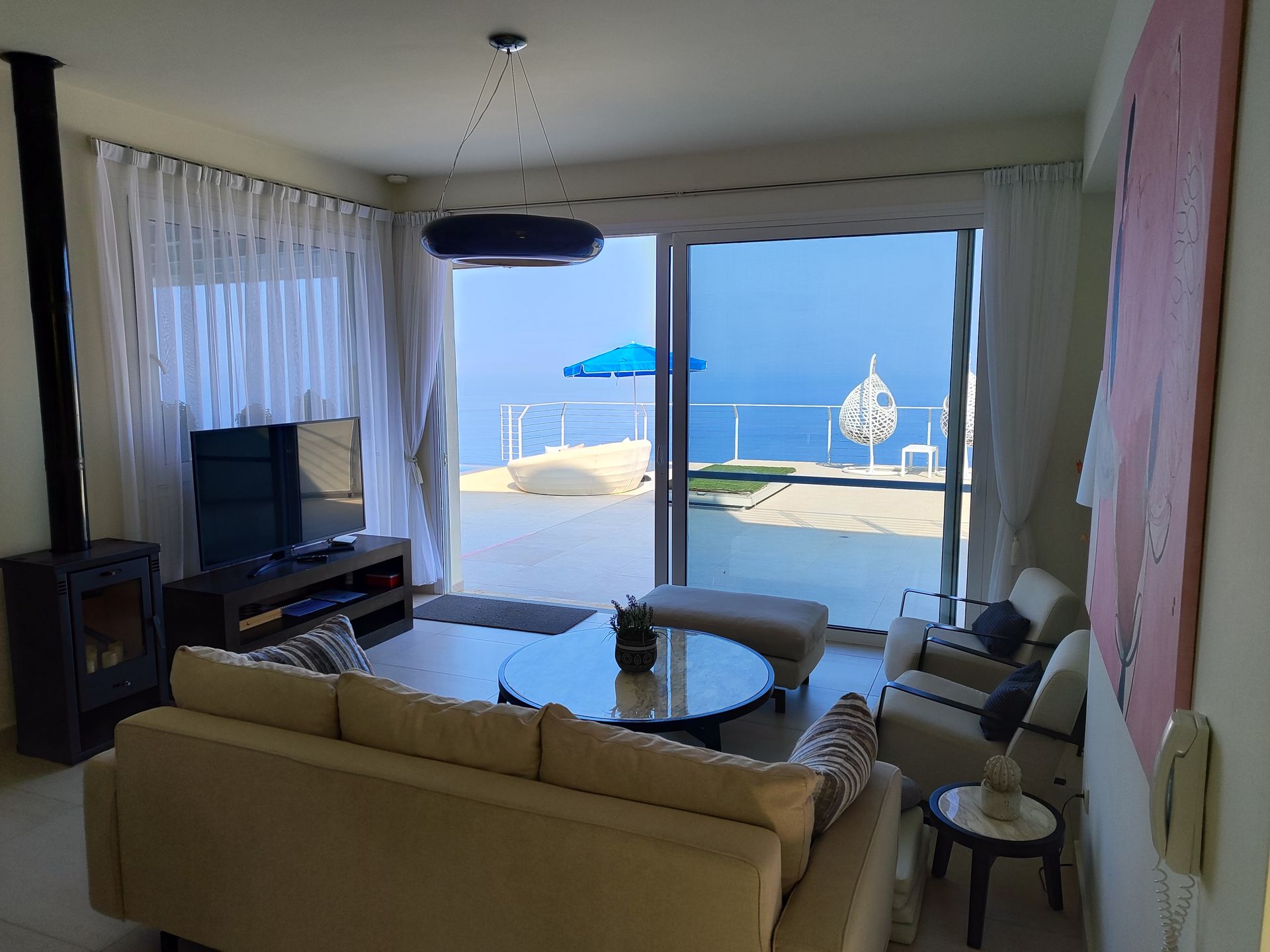 Living room with beige sofas and TV, opening to a patio and ocean view through large sliding doors