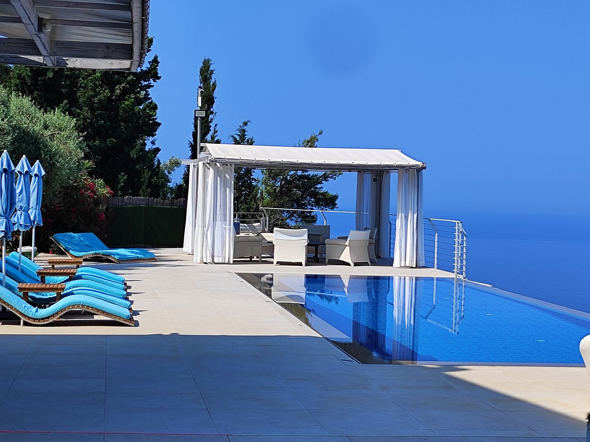 Luxury poolside cabana with white curtains, blue lounge chairs, and an ocean view