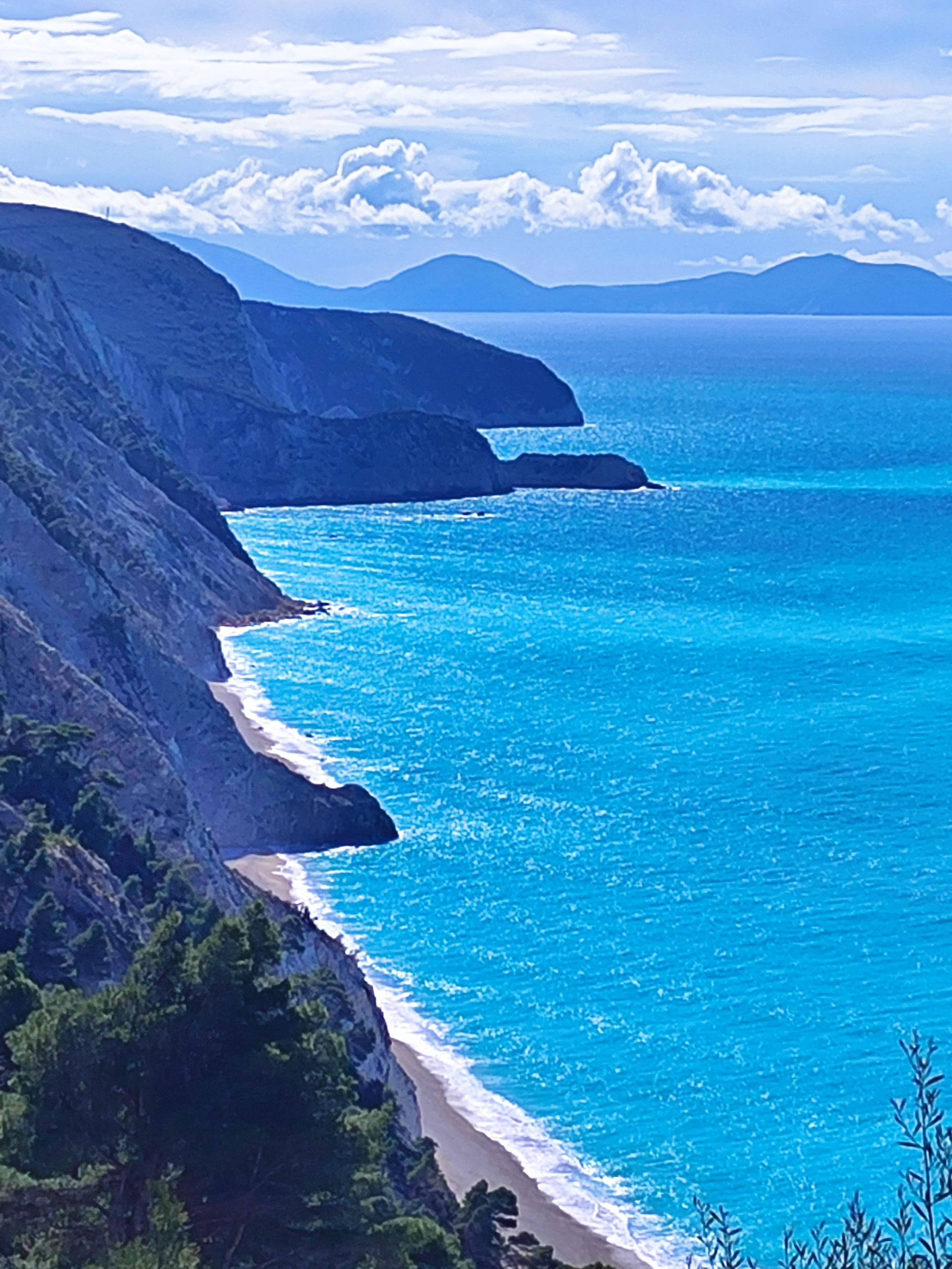 Blue ocean beside steep coastal cliffs and a sandy beach under a cloudy sky