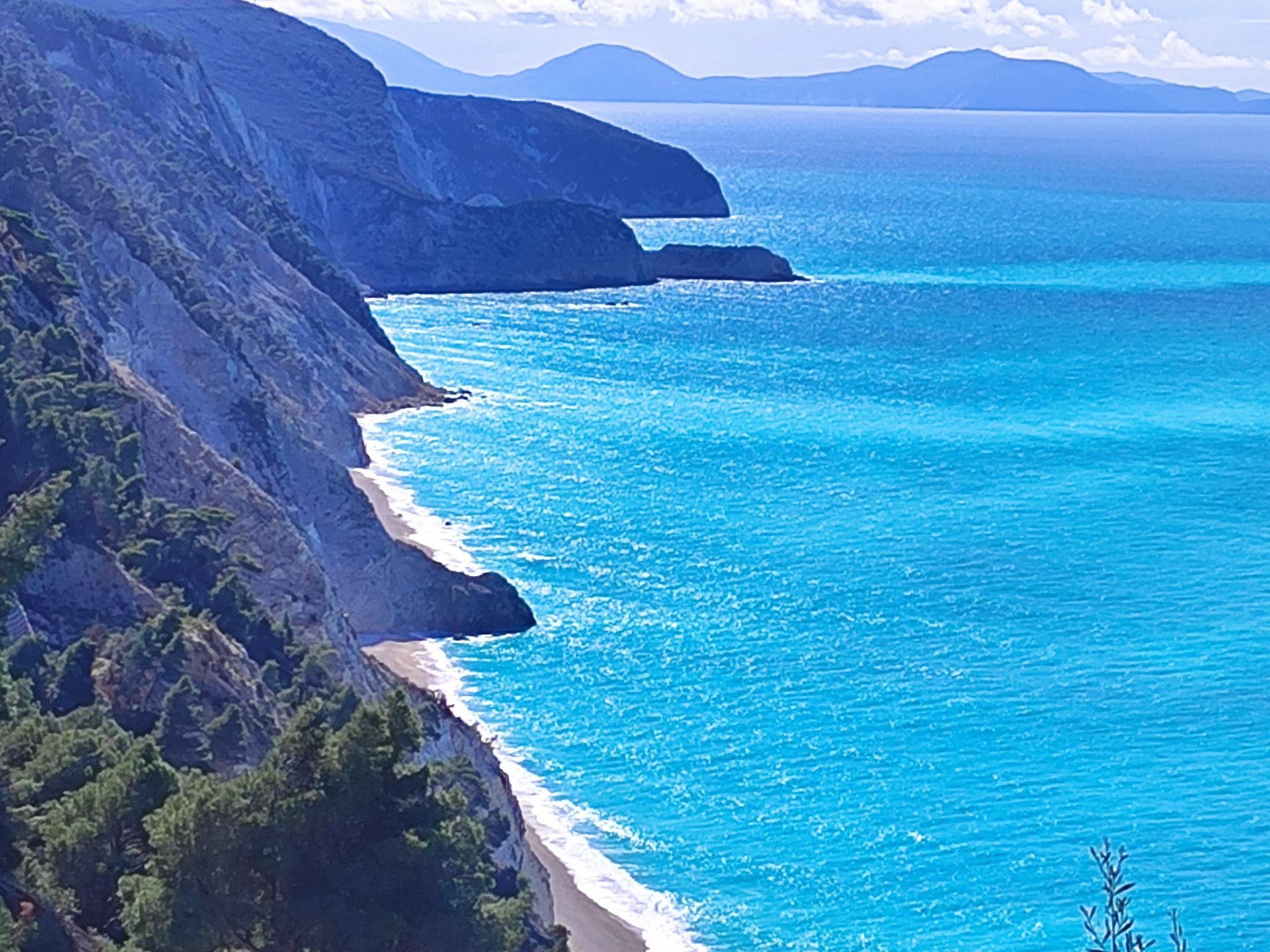 Rocky seaside cliffs beside bright turquoise water and a distant blue coastline