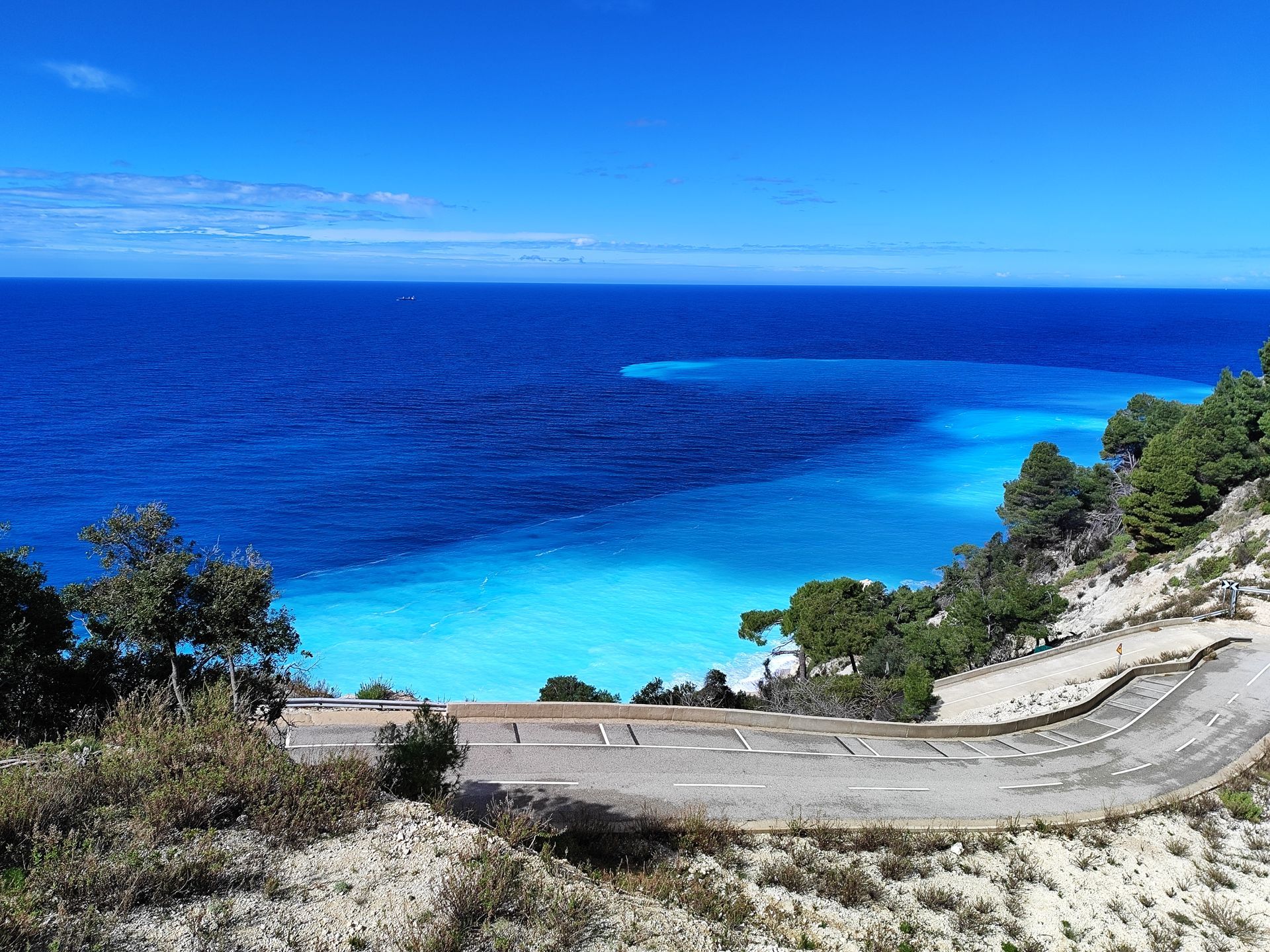 Coastal road overlooking a bright turquoise bay and deep blue sea under a clear sky