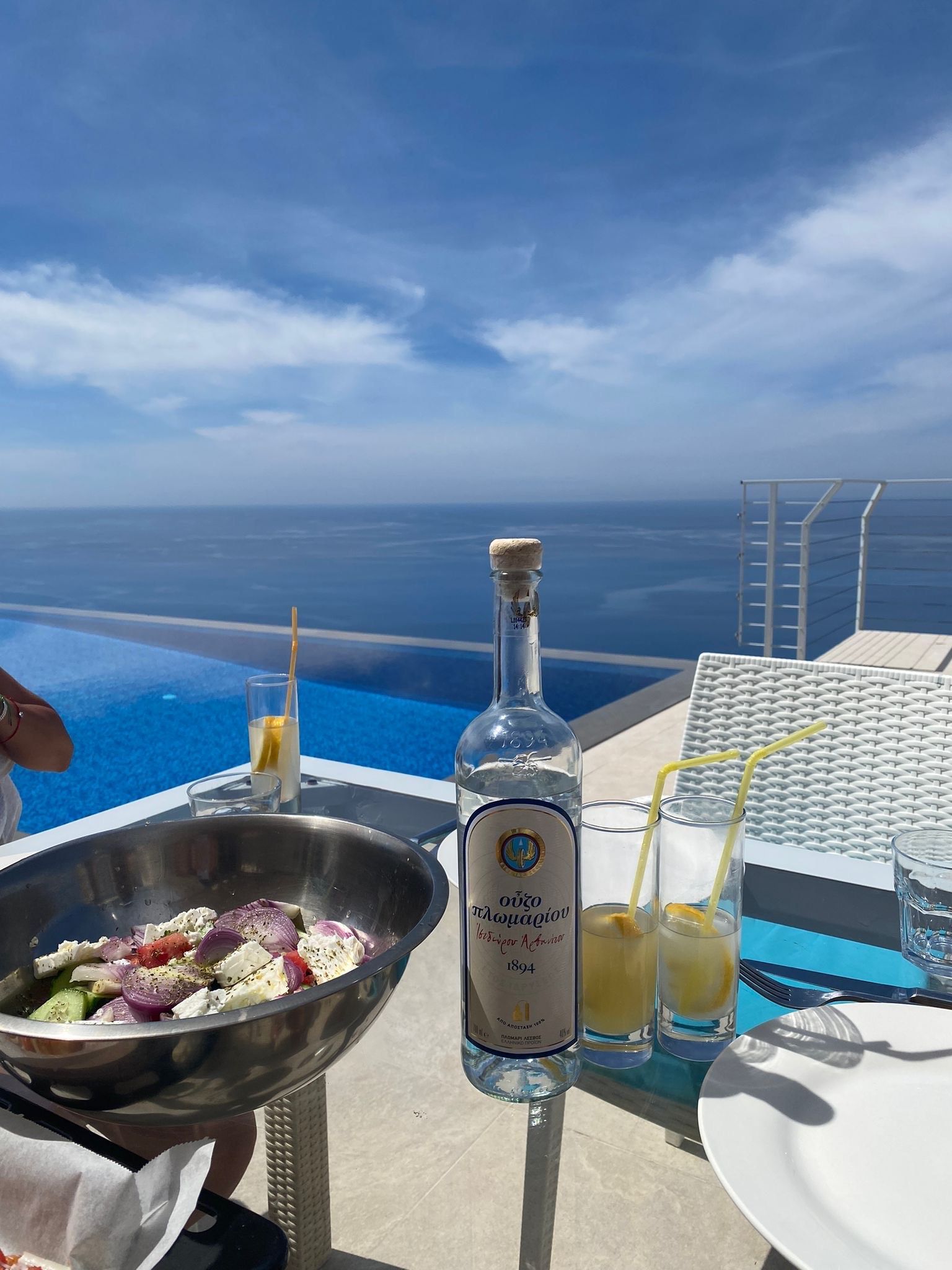 Seaside restaurant table with salad, drinks, and ocean view under a blue sky