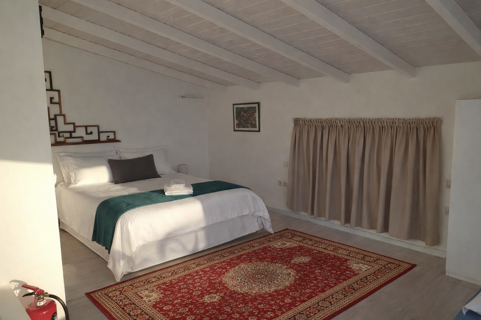 Small attic bedroom with a bed, red rug, and beige curtains under a sloped ceiling