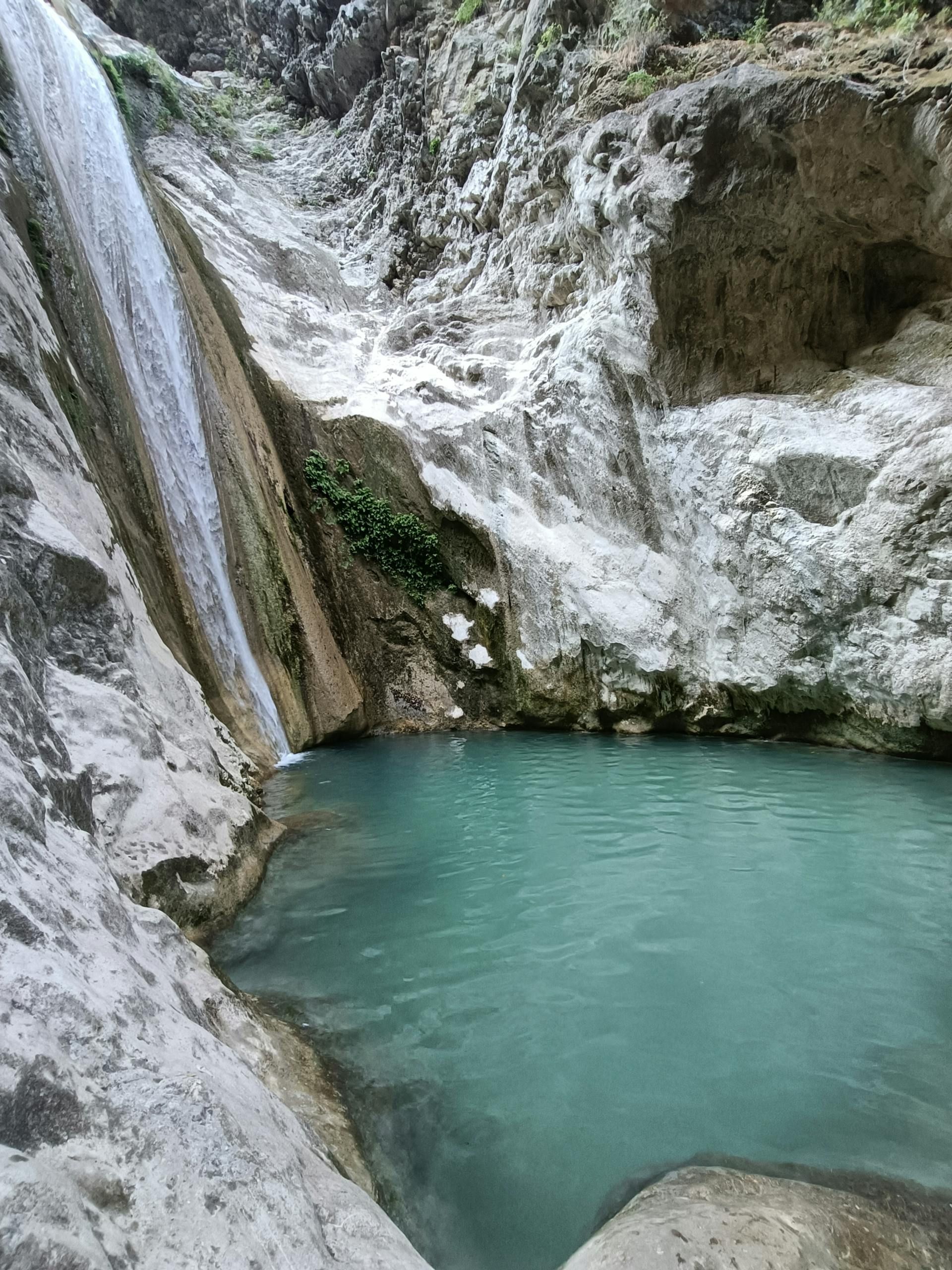 Turquoise mountain pool beneath a rocky waterfall and white limestone cliff