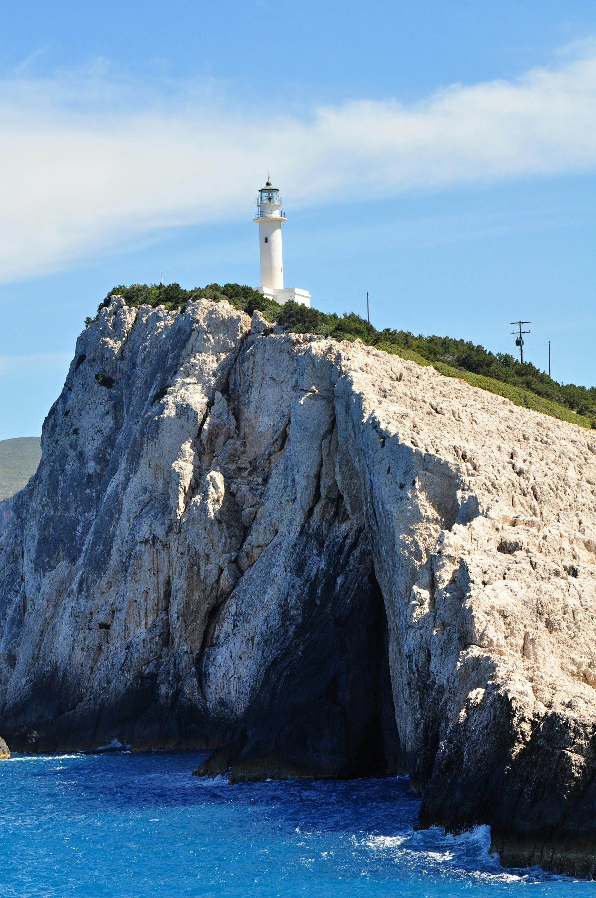 White lighthouse on a rocky cliff above deep blue sea under a clear sky