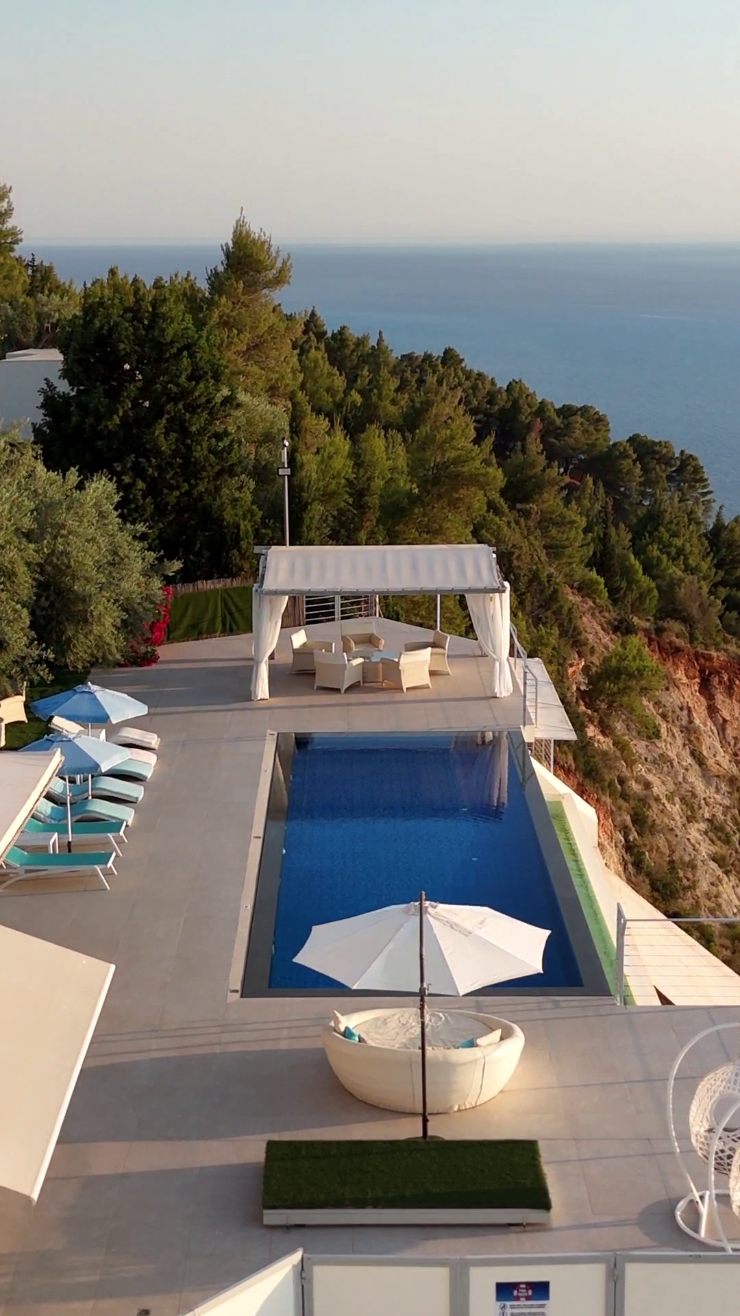 Infinity pool overlooking the sea, with lounge chairs and a white canopy on a sunny terrace