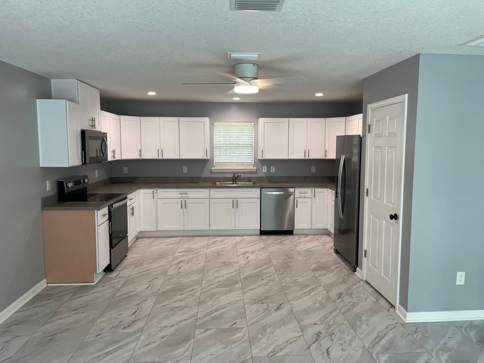 Empty gray kitchen with white cabinets, stainless appliances, and light wood-look flooring
