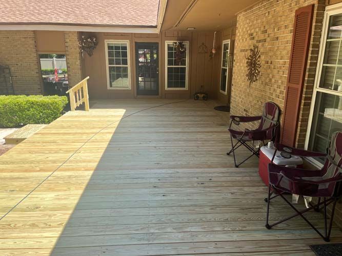 Covered wooden porch with two chairs beside a brick house and glass doors