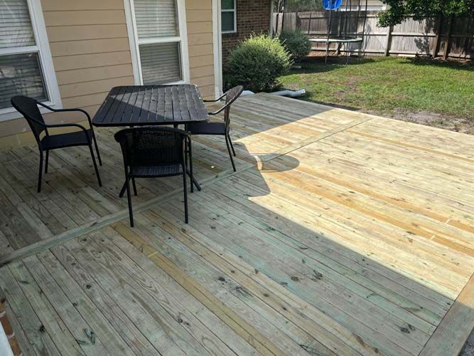 Outdoor patio with a black table and chairs on a weathered wooden deck beside a house