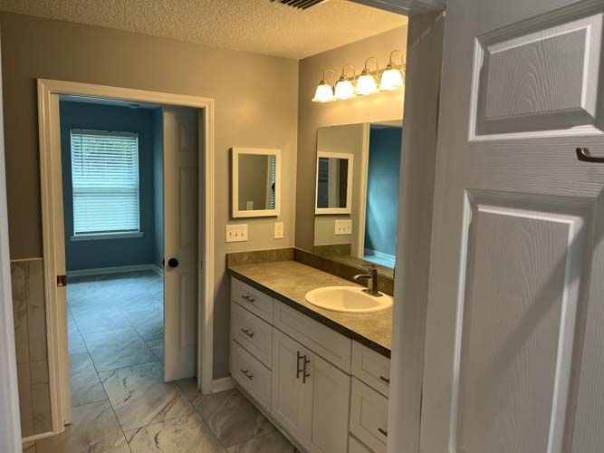 Bathroom vanity with beige cabinets, white sink, mirror, and doorway to a tiled room