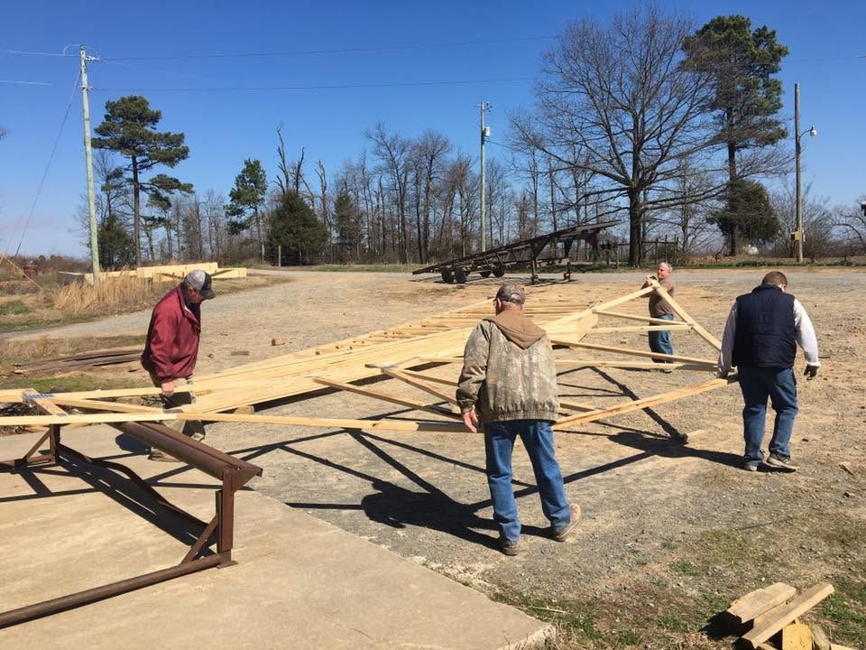 People assembling a large wooden structure outdoors on a bare field.