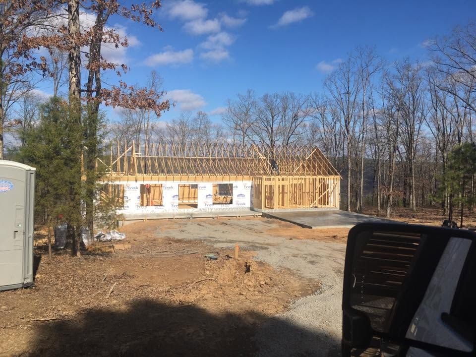 Partially built house with exposed framing on a dirt lot under a clear blue sky