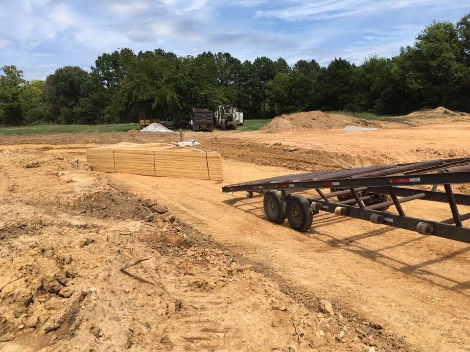 Cleared construction site with sandy ground, trees in back, and a trailer in the foreground
