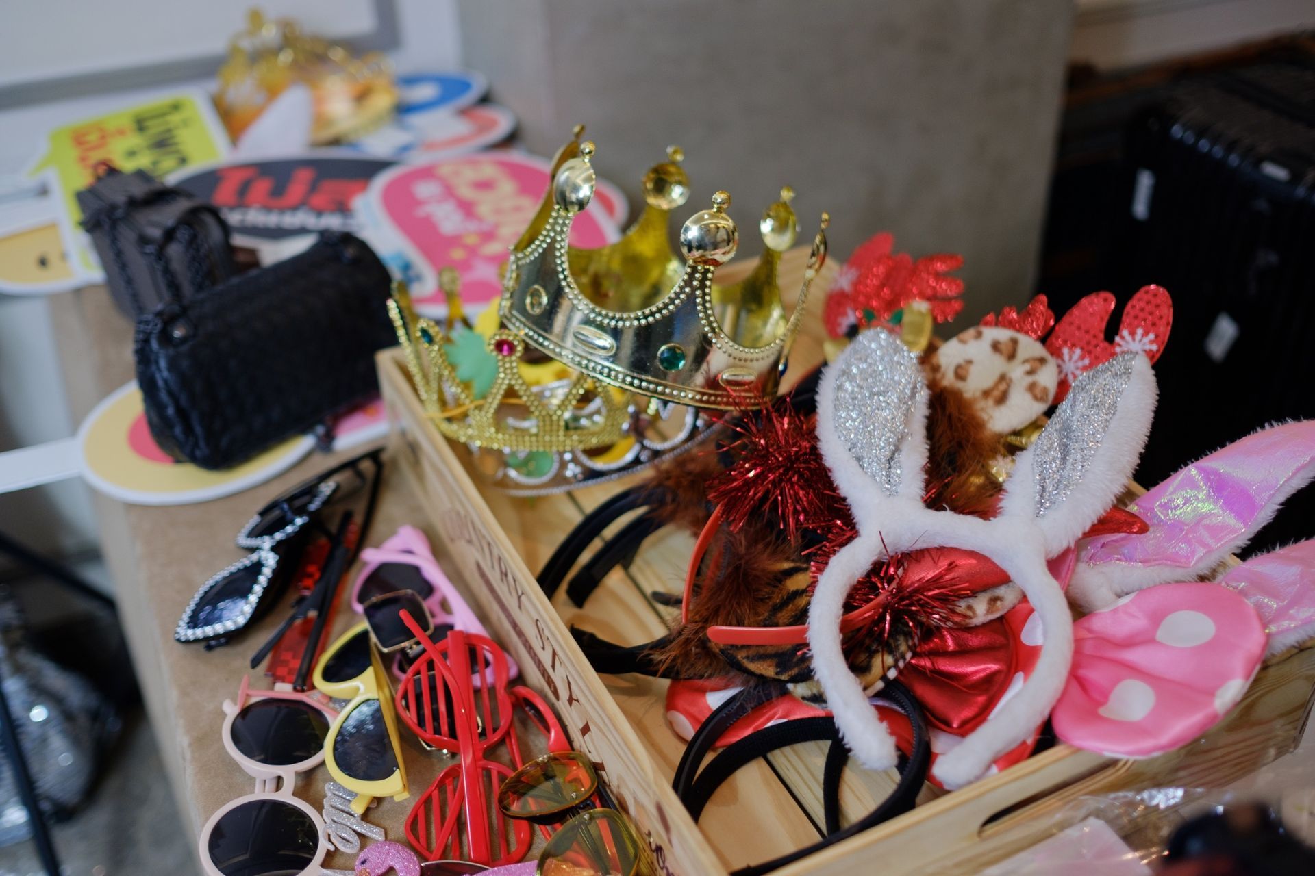 A wooden crate filled with party props, including gold crowns, heart-shaped glasses, and bunny ear headbands.