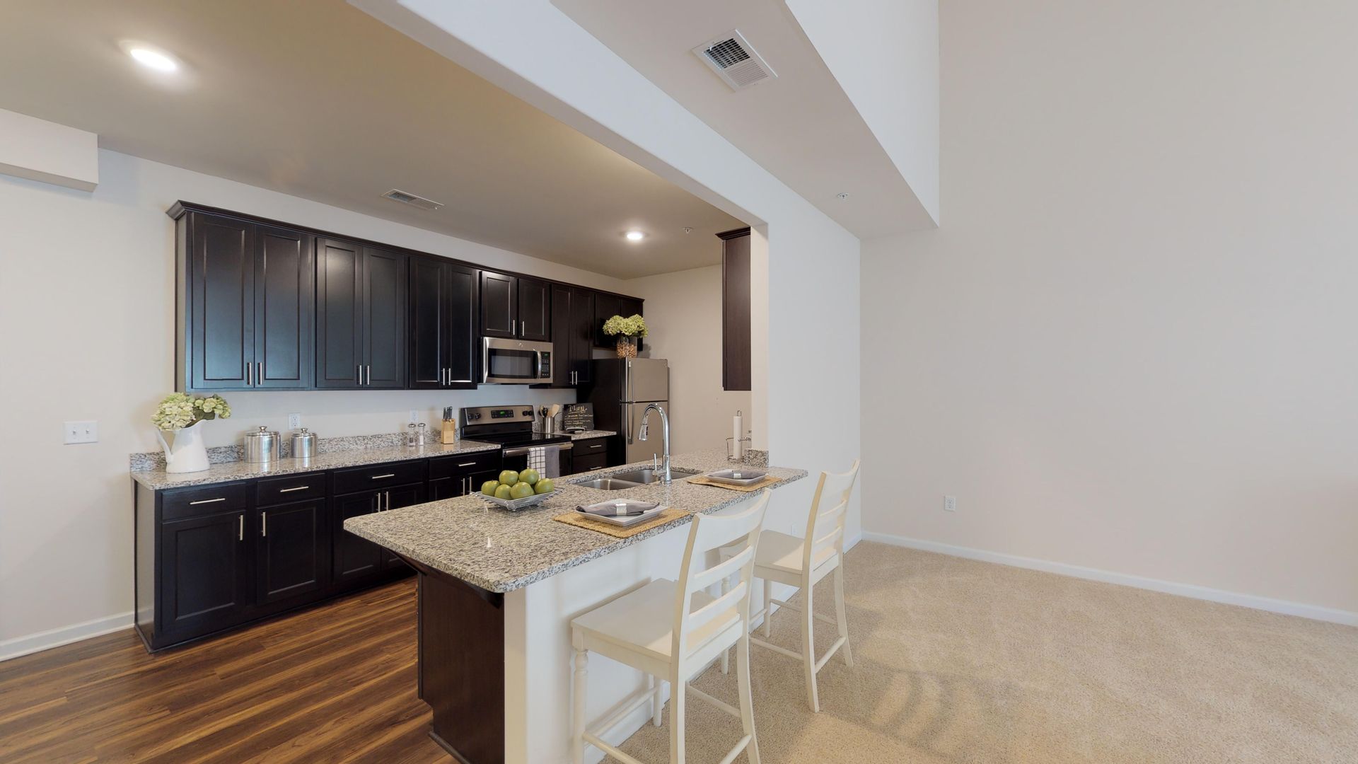 A kitchen with black cabinets , granite counter tops , stainless steel appliances and a large island.