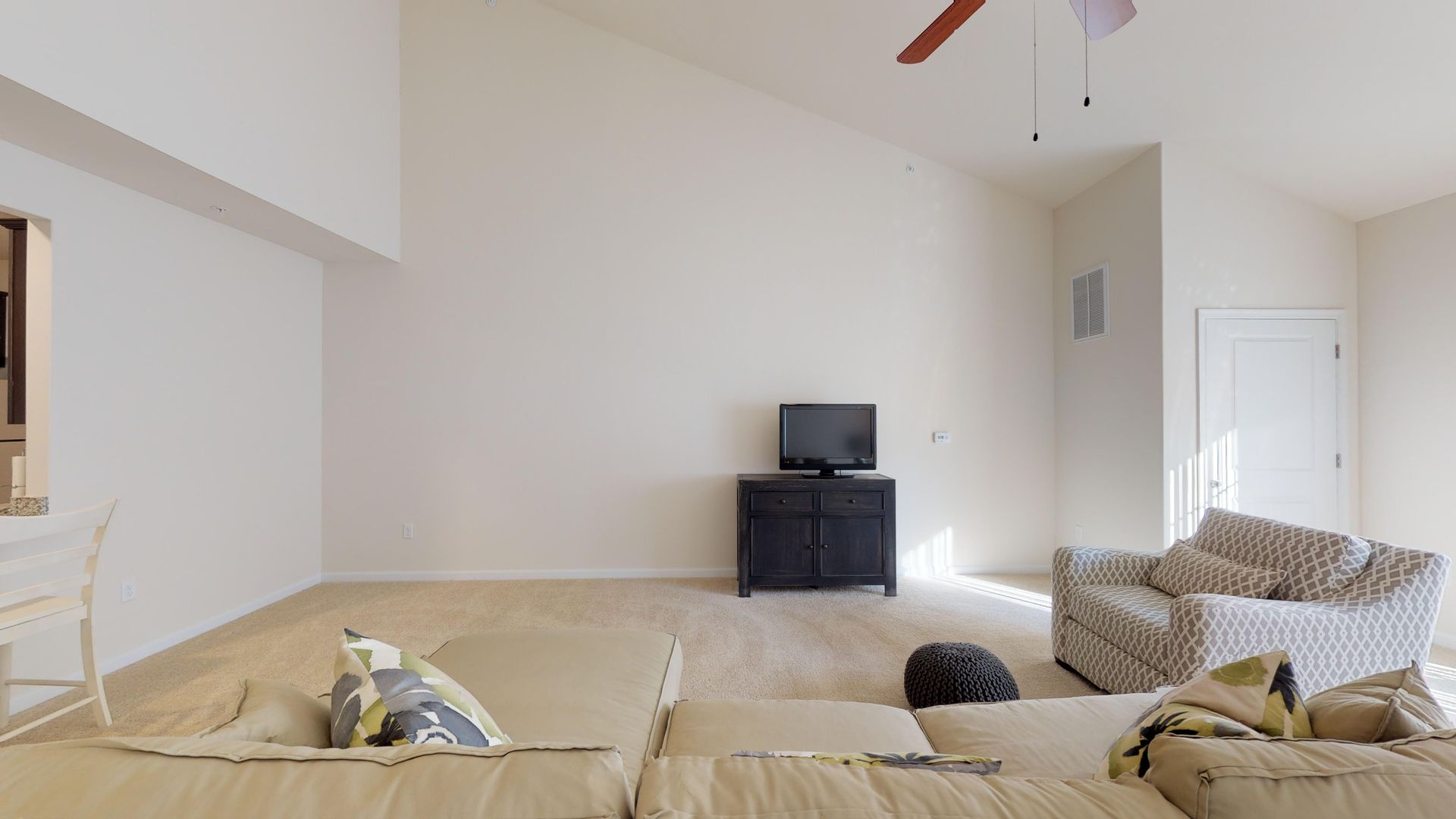 A living room with a couch , chair , television and ceiling fan.
