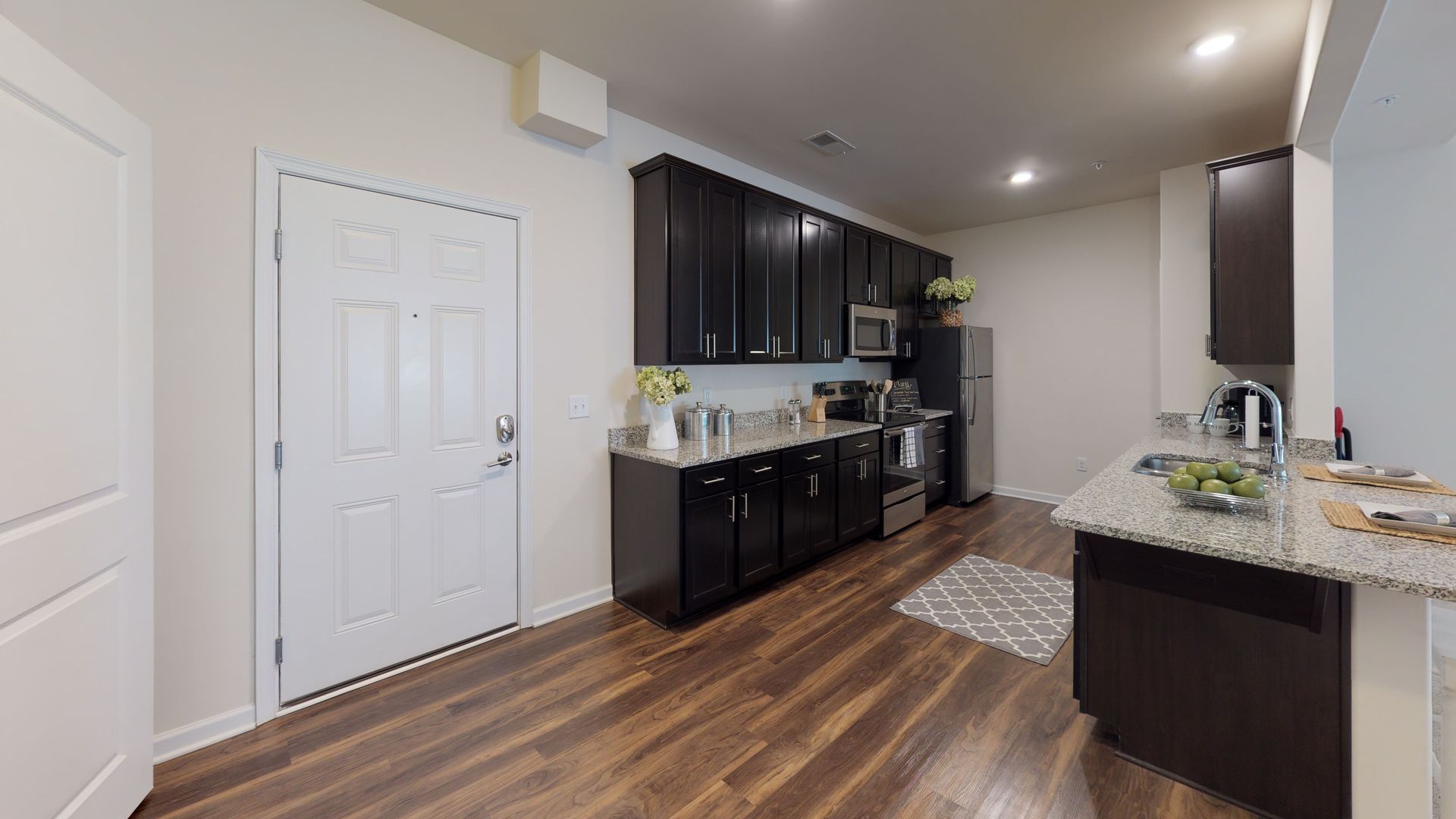 A kitchen with black cabinets , granite counter tops , stainless steel appliances and hardwood floors.