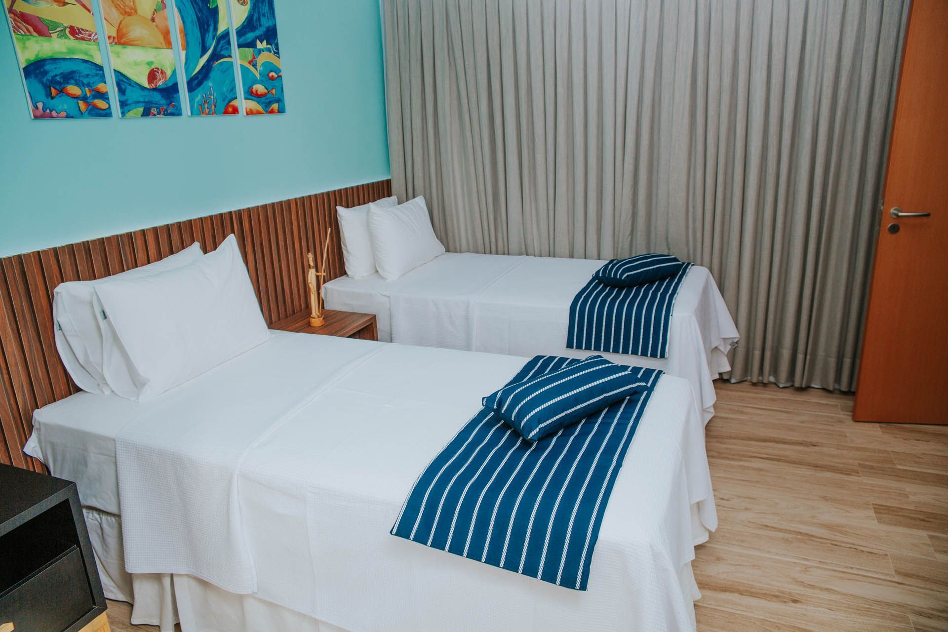 Duas camas de solteiro com cobertores listrados de azul em um quarto arrumado com cortinas e piso de madeira.