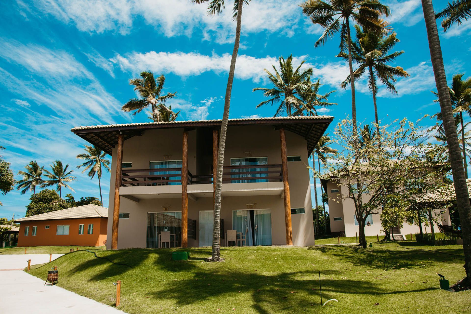 Prédio de um resort tropical com varanda coberta, palmeiras e um céu azul brilhante.
