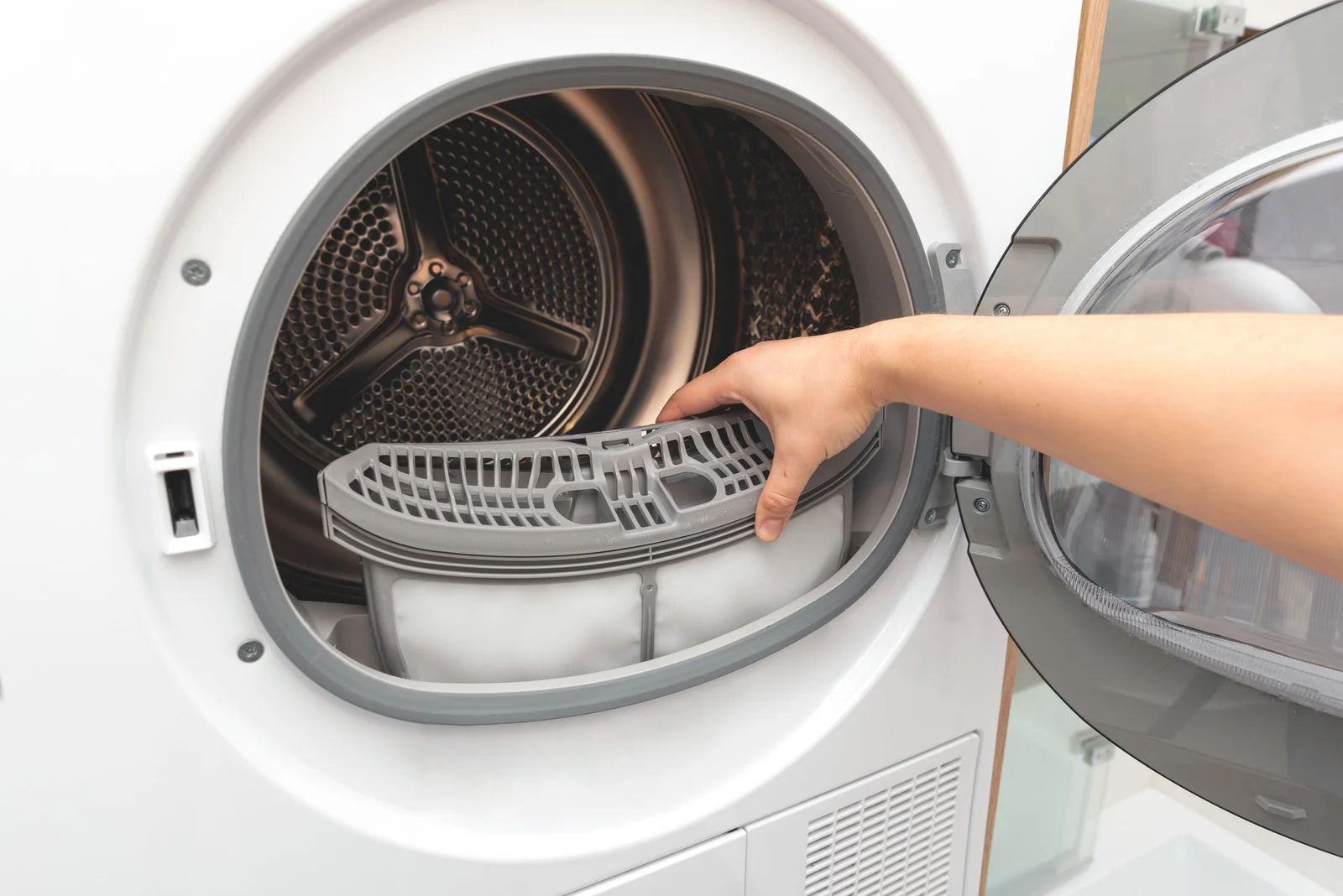 Hand placing a lint filter into an open front-load dryer drum