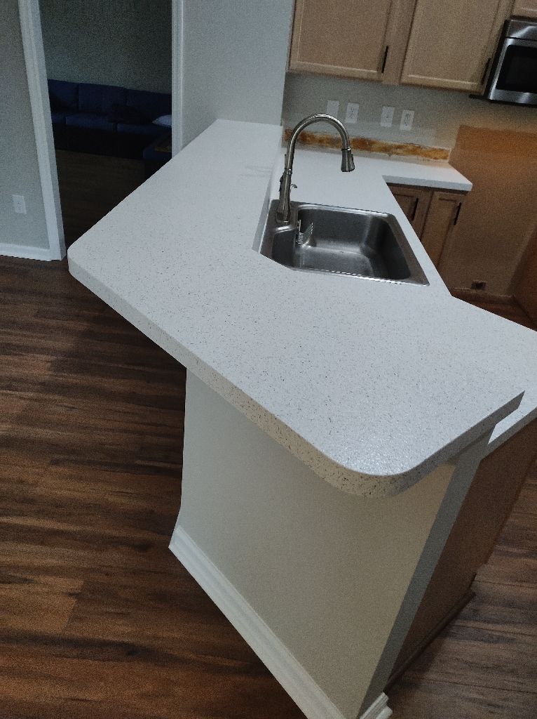 Empty kitchen island with stainless-steel sink and faucet in a room with dark wood floors.