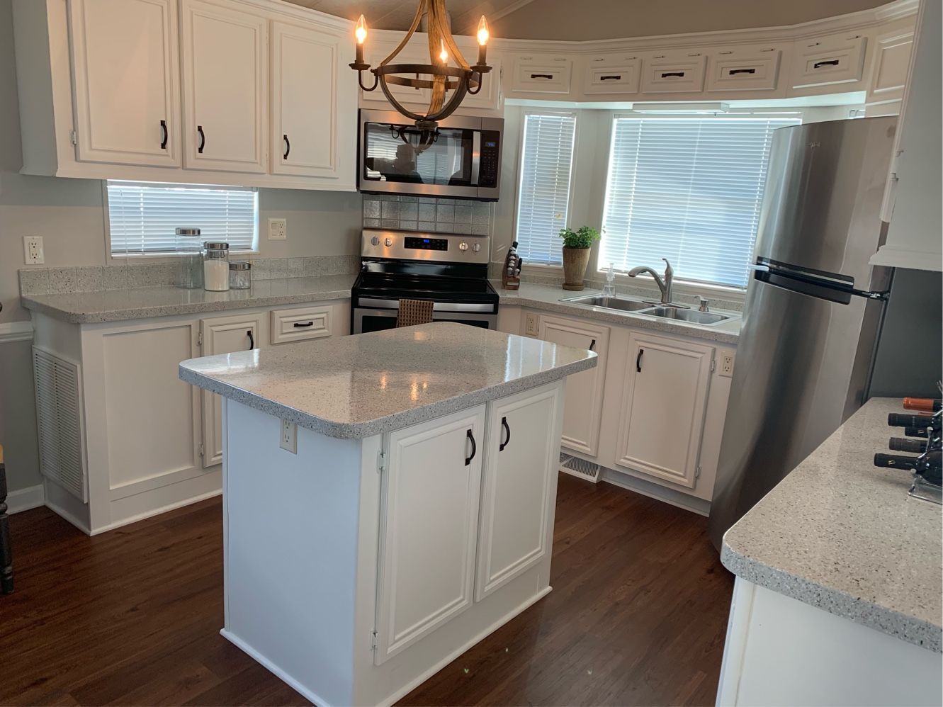 Bright white kitchen with an island, stainless steel appliances, wood floor, and bay window.