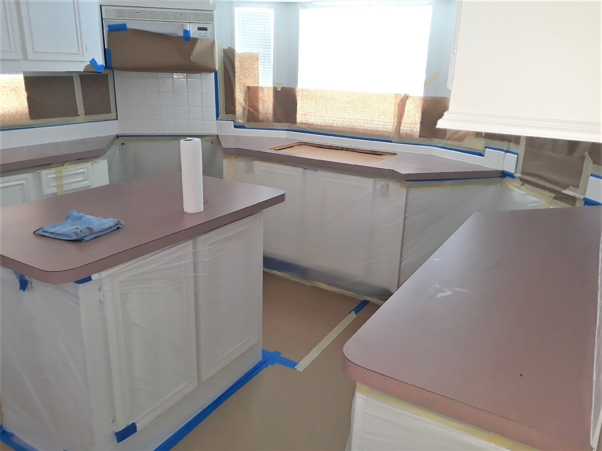 Empty kitchen with white cabinets, pink countertops, and blue painter’s tape around the floor edges.