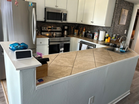 Small kitchen with white cabinets, stainless appliances, and a beige tiled breakfast bar counter.