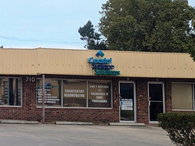 Small brick office building with a beige awning and blue sign, front windows, and a glass door.