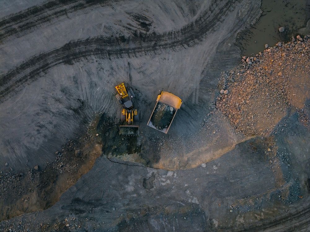 Two yellow construction trucks on a gravel quarry road, viewed from above.