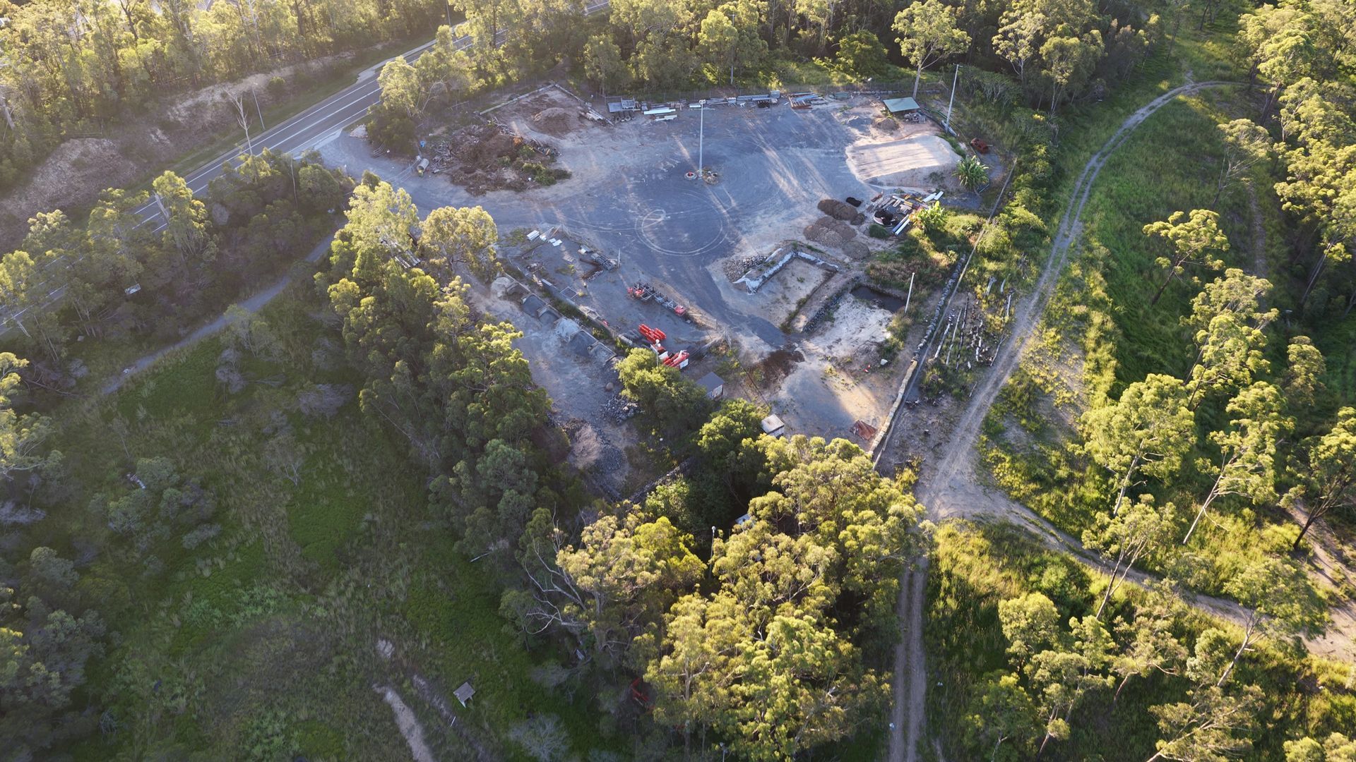 Aerial view of a wooded site with a large cleared gravel area and dirt roads.