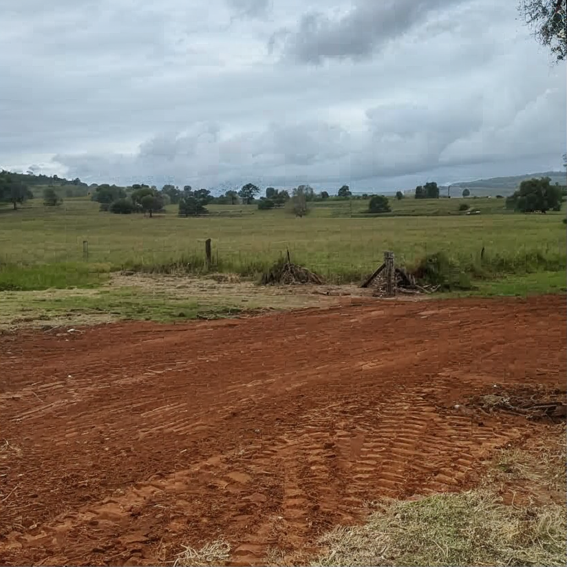 Red dirt road beside grassy fields under a cloudy sky