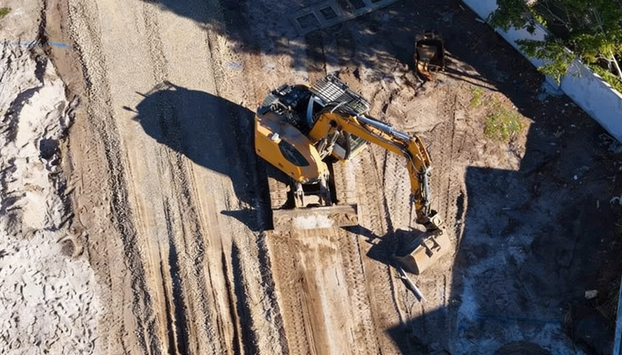 Yellow excavator digging in a dirt construction site beside a paved road