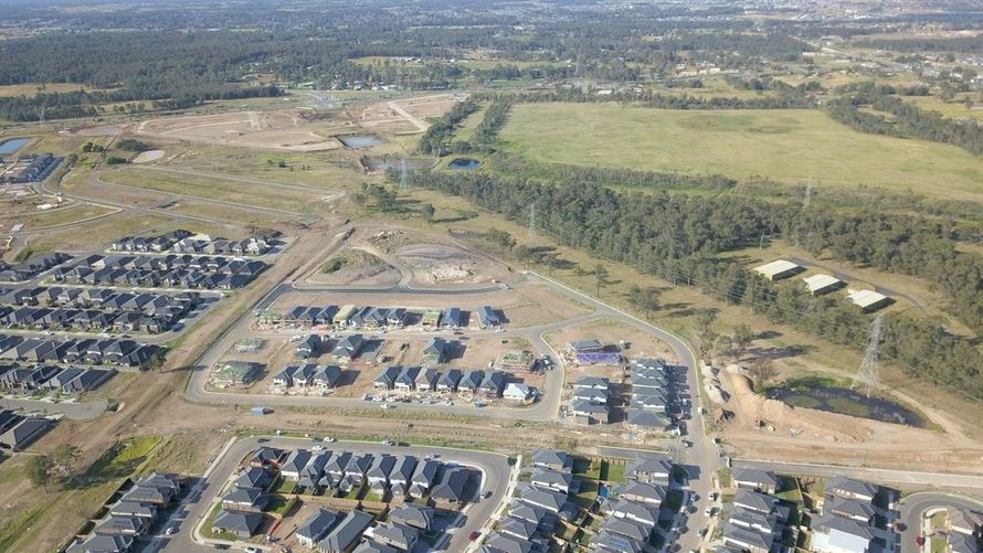 Aerial view of a large suburban housing development with roads, construction sites, and open fields.