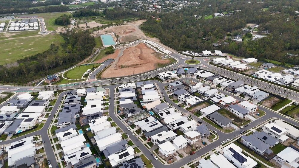 Aerial view of a suburban housing development with white-roofed homes and a large construction site nearby