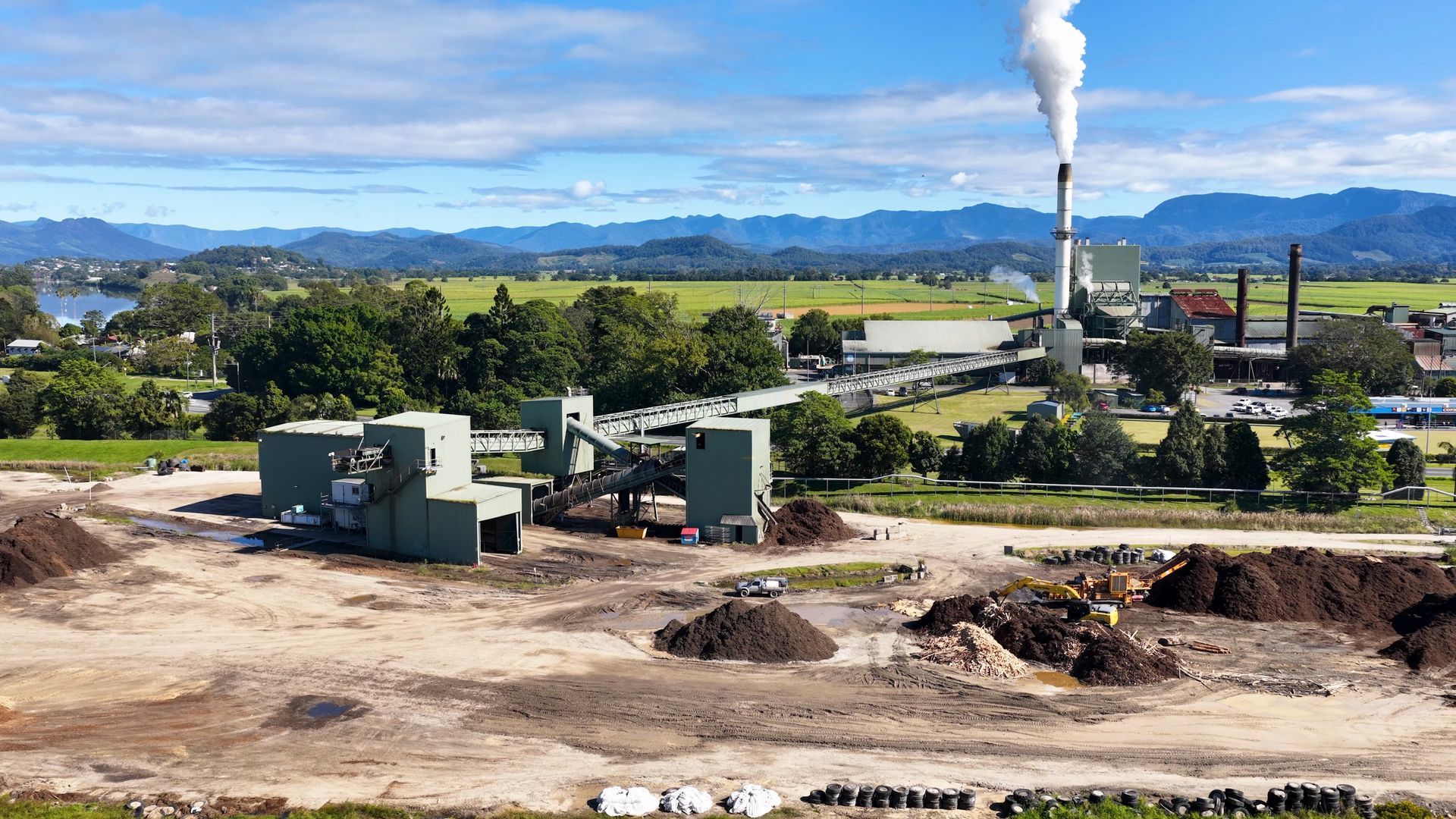 Industrial facility with smoke stack near a rural landscape and mountains in the distance