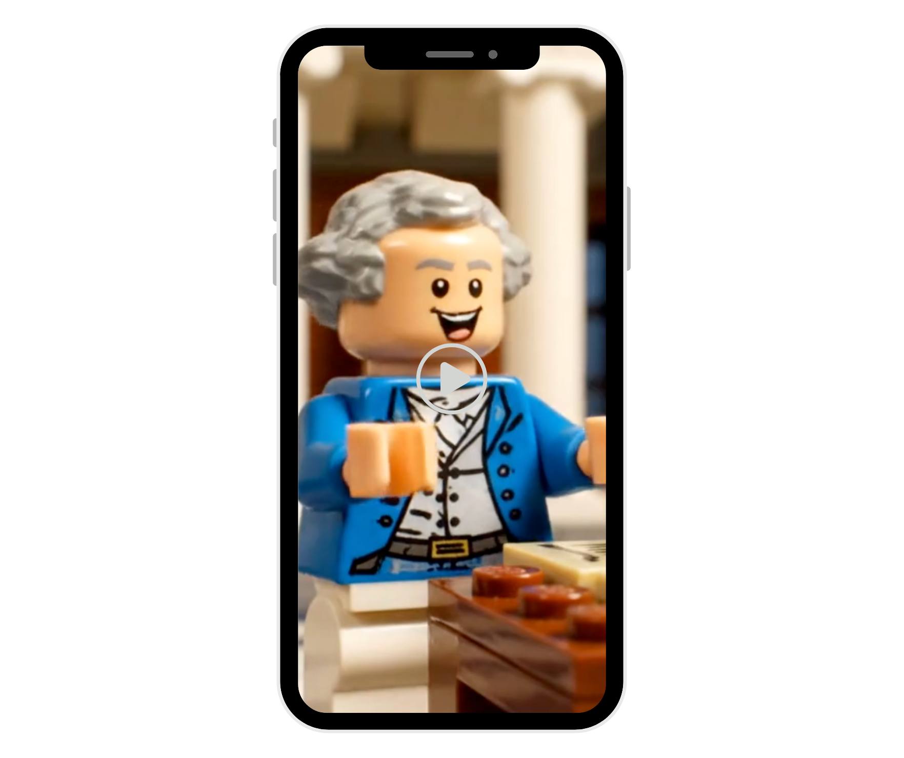 A Lego figure in a colonial-style blue coat and wig smiles inside a smartphone screen, overlaid with a play button.