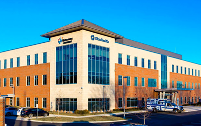 Exterior of OhioHealth building with brick and blue accents, parked vehicles, and a clear sky.