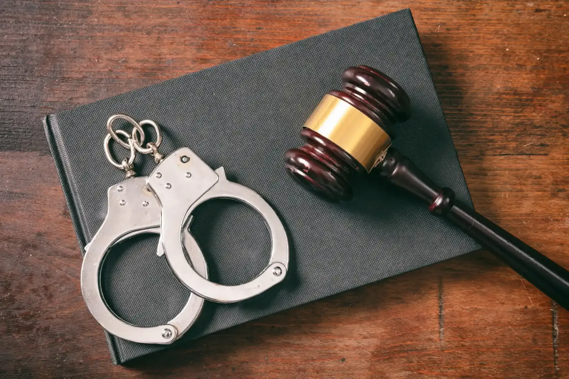 Handcuffs, gavel, and book on a wooden surface, suggesting legal proceedings.