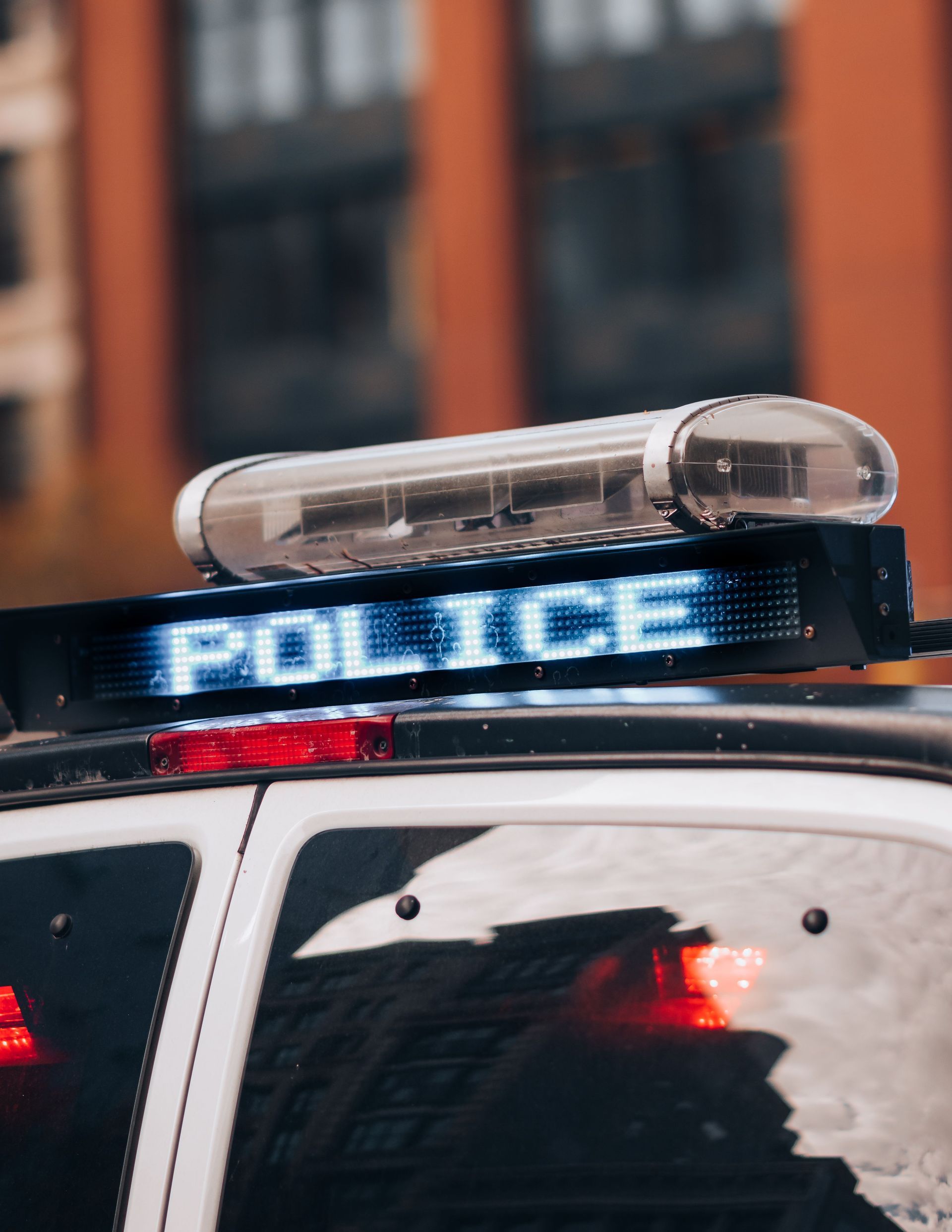 Close-up of a police car roof with flashing blue lights and a light bar in an urban setting