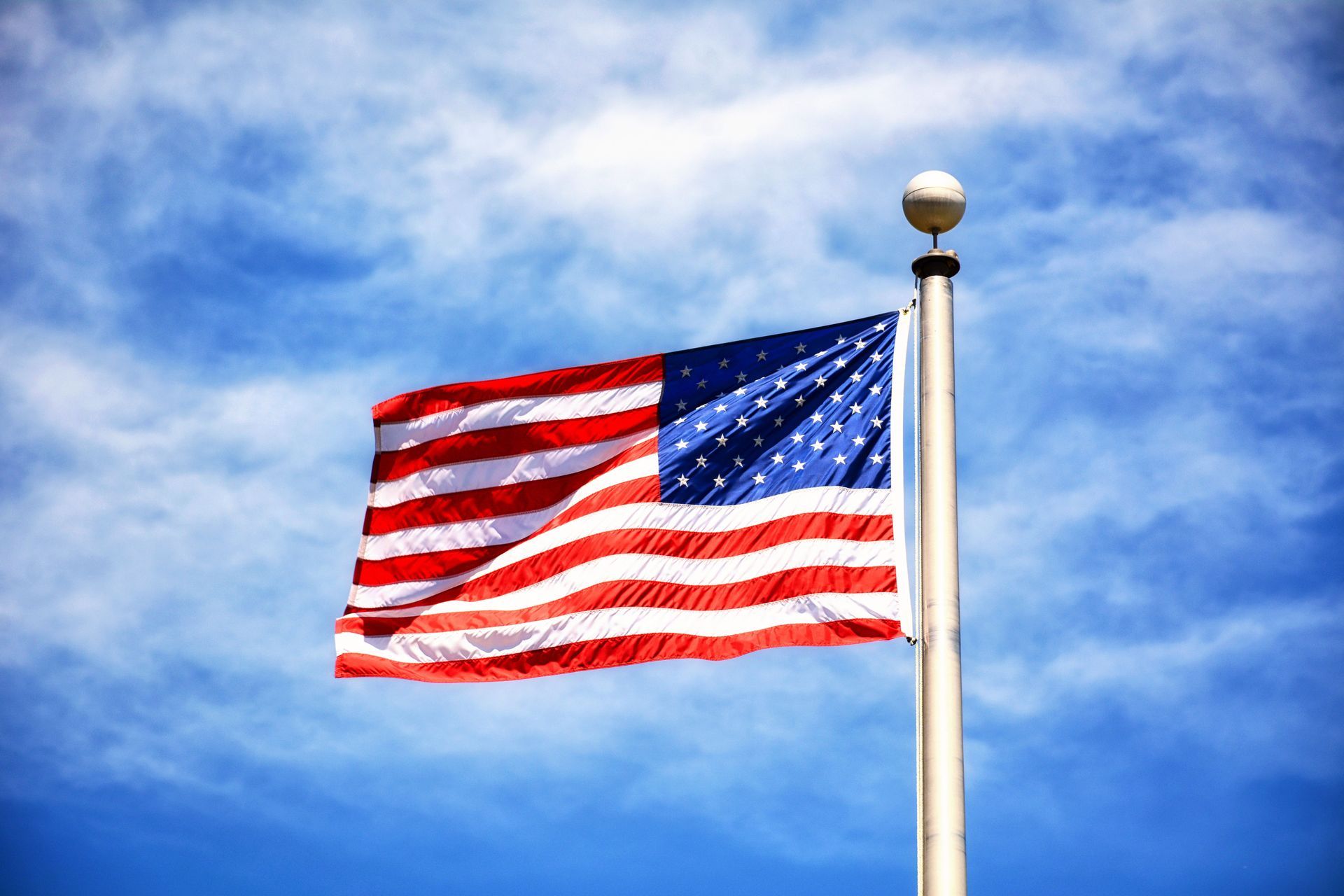 American flag waving on a pole against a blue cloudy sky