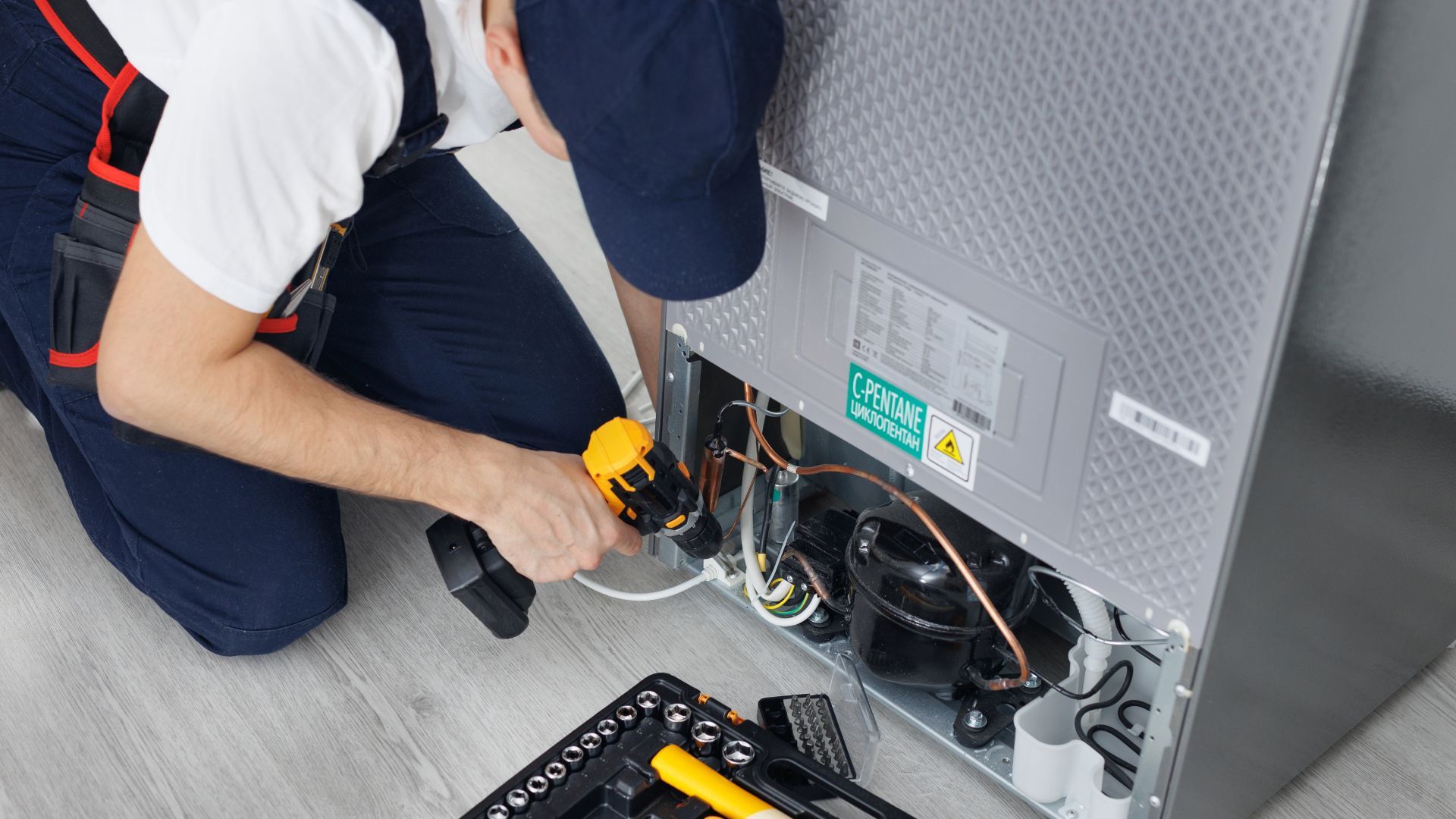 A man is fixing a refrigerator with a screwdriver.