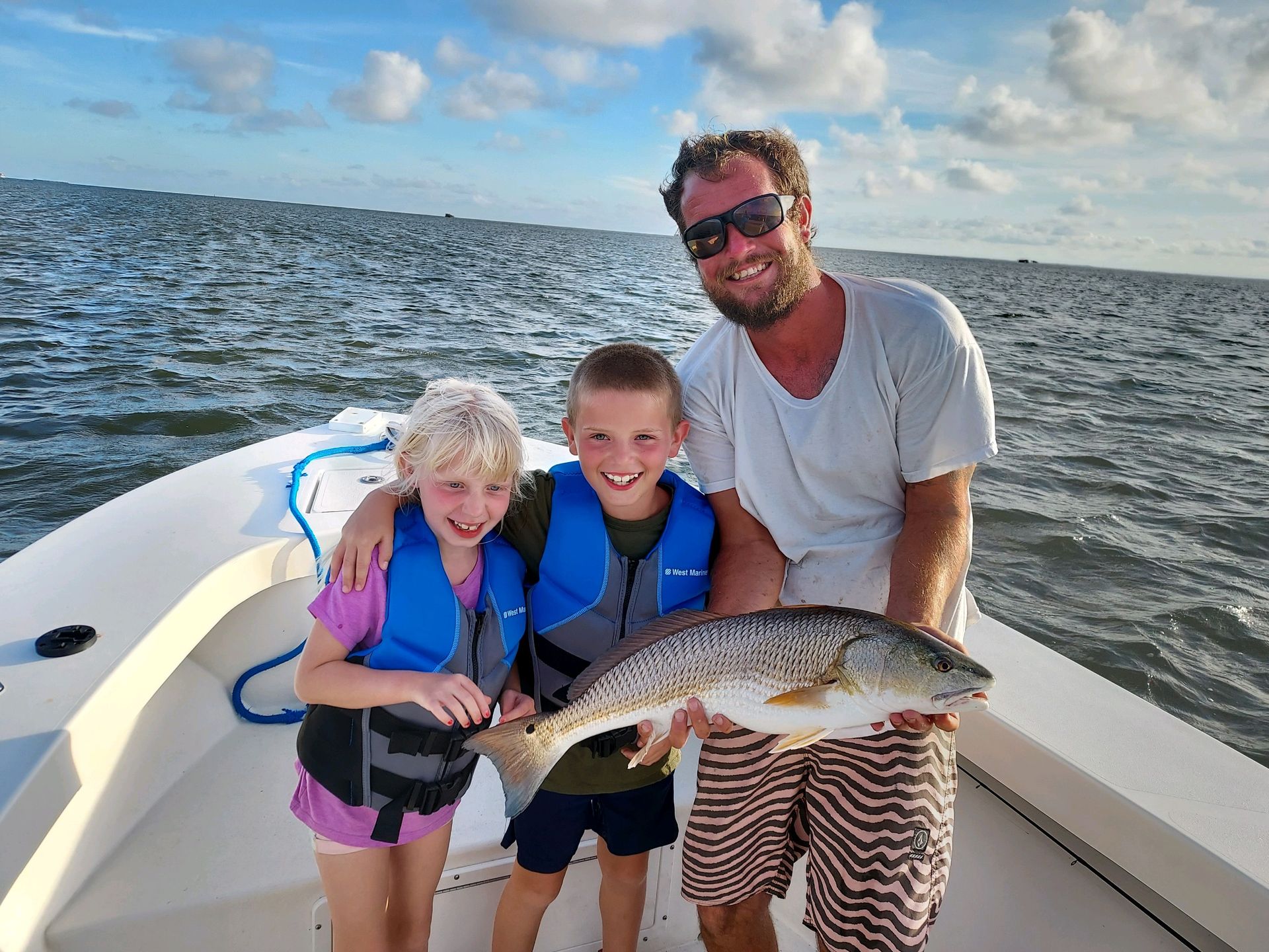 Three people on a boat holding a large fish on a sunny day at sea