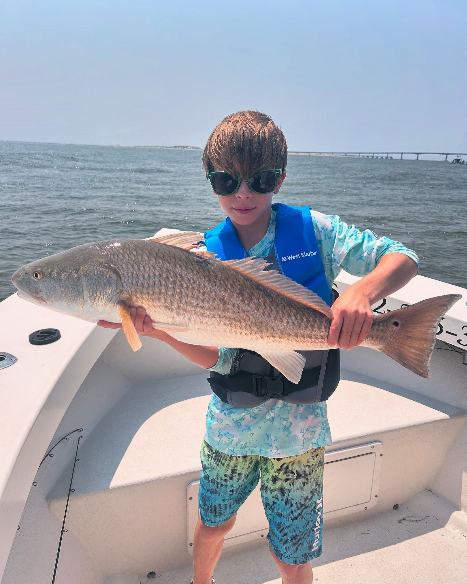 Child on a boat holding a large fish on a sunny day