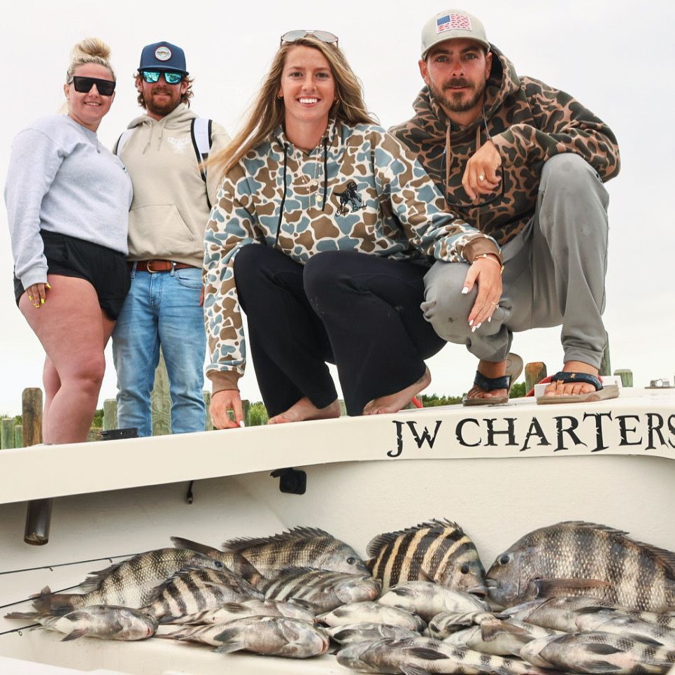 Four people pose on a charter boat above a catch of striped fish on deck.