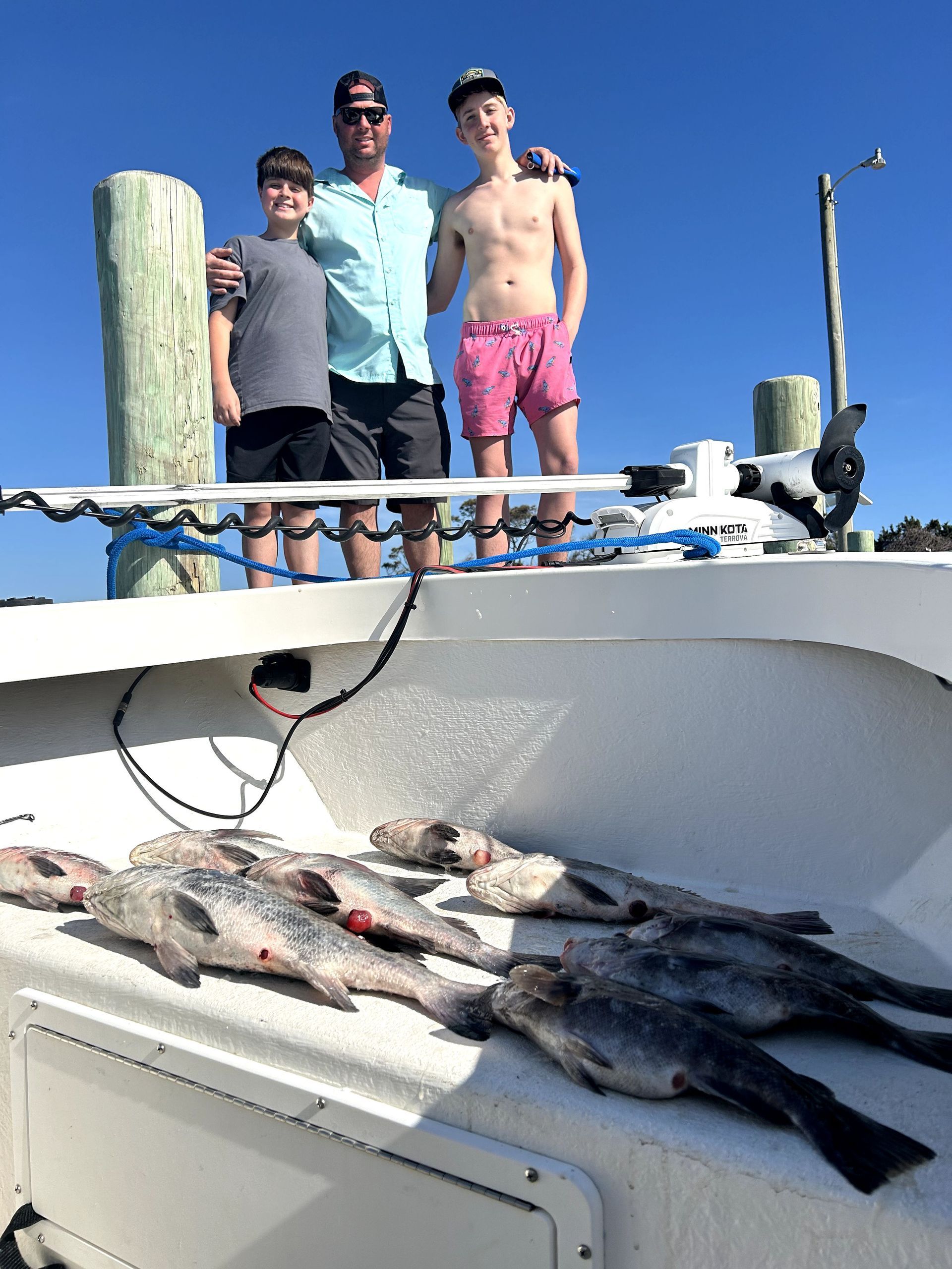 Three people on a boat dock with several large fish laid out in the foreground.
