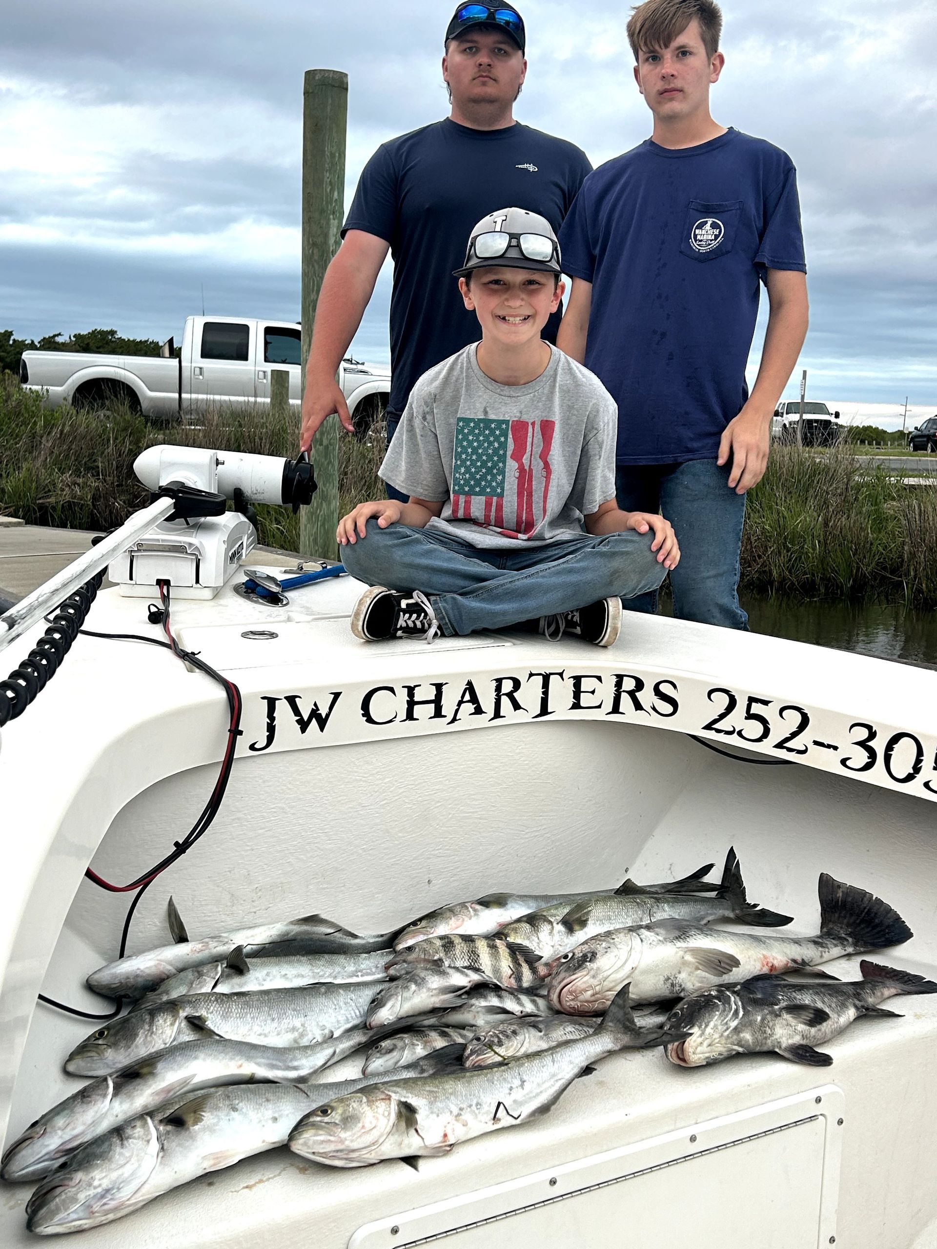 Three people on a charter boat with a large catch of fish displayed on the deck
