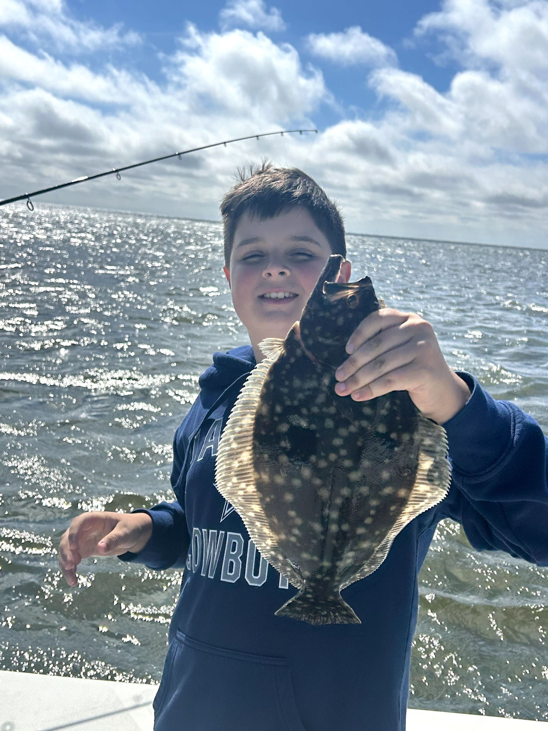 Person holding a fish on a boat by the water under a cloudy sky